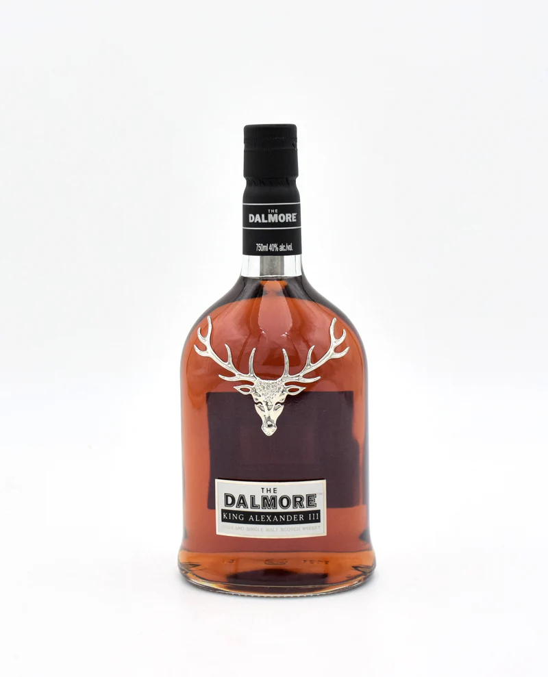 Dalmore Alexander Cask King Alexander III single malt bottle featuring its iconic silver 12-point royal stag emblem nested inside a sleek open display presentation case showing a historic monochromatic illustration.